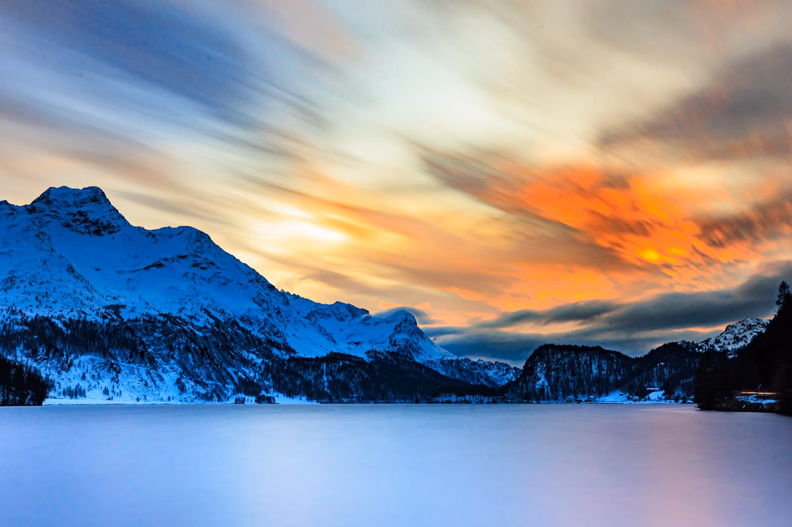 Verschneite Berge und gefrorener See unter einem feuerroten Wolkenhimmel